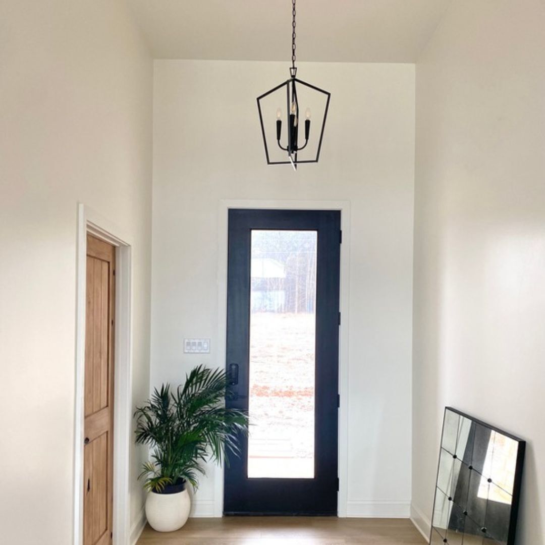 A black, geometric lantern-style chandelier hangs from a chain in an entryway. The fixture features a five-sided open frame with three exposed candelabra-style light bulbs in the center.